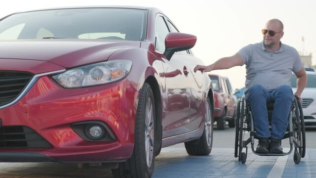Young handicapped driver getting in red car from wheelchair