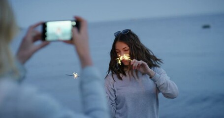 sparkler woman dancing loop girl using smartphone taking photo of friend dance with sparklers on beach at sunset celebrating new years eve sharing independence day celebration on social media - Powered by Adobe