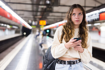 Beautiful young woman with smartphone, standing on the platform of metro underground station