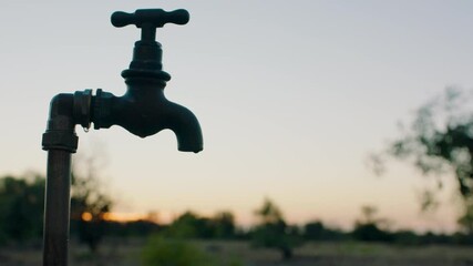 water dripping from tap on rural farm at sunset freshwater drips from faucet outdoors wasting water shortage on farmland drought