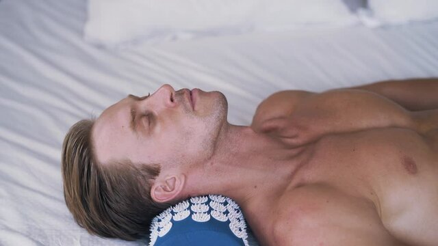 Caucasian man has a pain in his neck and lays on spiky mat. Sporty man lays down on acupuncture applicator and spiked pillow. He feels comfortable. Healthy lifestyle. High quality 4k footage.