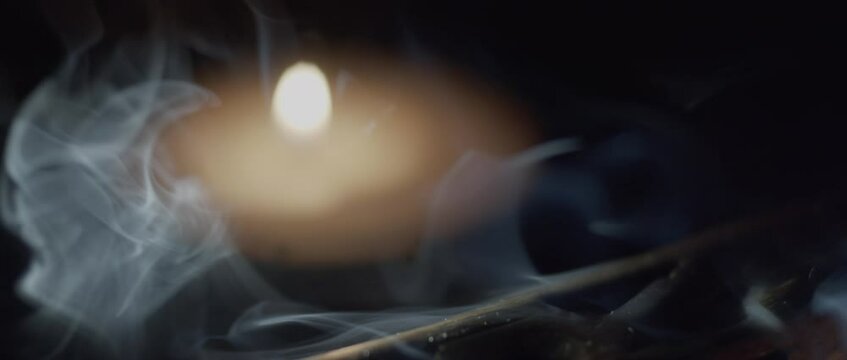 Beautiful slow motion of an incense smoke rising from a holder with candle burning in the background. Shallow depth of field. 