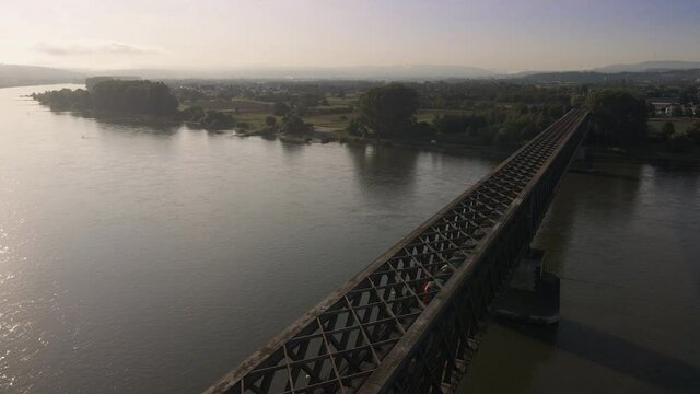 Aerial flight over Rhine river with train crossing Urmitzer Bridge, Germany