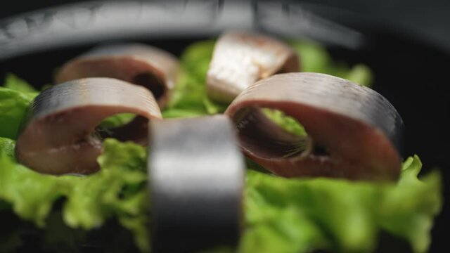 Close up herring in chunks with greens are rotating on the plate on black background. Healthy food clean eating selection.