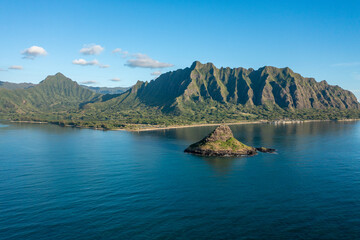 Aerial view of Chinaman's Hat in Oahu, Hawaii, with the Ko'olau mountain range in the background. Morning golden light with a few puffy white clouds in a blue sky.