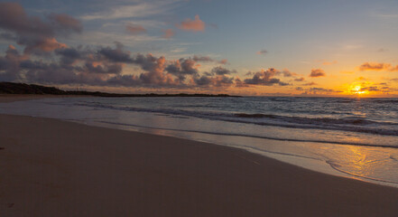 Hawaiian beach sunrise. Yellow, orange, and lavender hues in the sky, light cumulus clouds. 