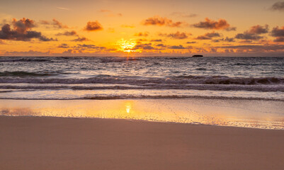 Fototapeta na wymiar Hawaiian beach sunrise. Yellow, orange, and lavender hues in the sky, light cumulus clouds. 