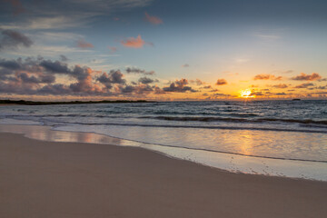 Naklejka na ściany i meble Hawaiian beach sunrise. Yellow, orange, and lavender hues in the sky, light cumulus clouds. 