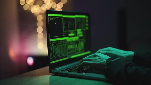 Hacker is working on laptop at night. Hands are typing a virus code at keyboard or hacking website. Closeup. Concept of bitcoin cryptocurrency and wallet hack. Software coder or blockchain developer