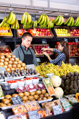 Fototapeta na wymiar Friendly positive smiling man and woman laying out vegetables and fruits in shop