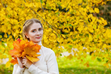 Woman in an autumn park. An emotional portrait of a cute and positive beautiful blonde girl with a bouquet of maple leaves on a background of blurred yellow foliage