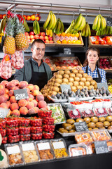 Friendly positive man and woman laying out vegetables and fruits in shop