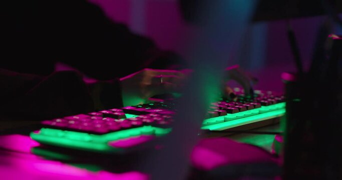 computer hands typing on keyboard hacking data on internet cyber crime information hack by anonymous hacker using rgb gaming keyboard with green backlight