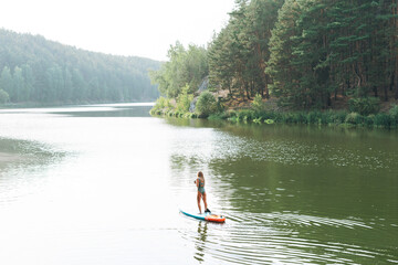 Fototapeta na wymiar The slim young woman in green sweemsuit on sup boat with oar floating on river, weekend trip and local travel