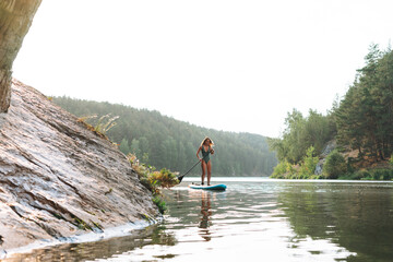 The slim young woman in green sweemsuit on sup boat with oar floating on the river, weekend trip...