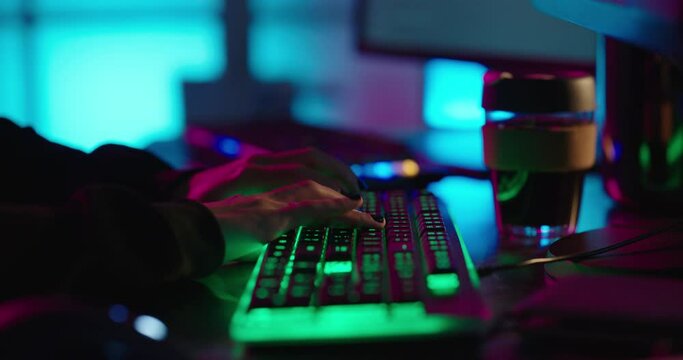 computer hands typing on keyboard hacking data on internet cyber crime information hack by anonymous hacker using rgb gaming keyboard with green backlight