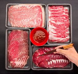 Chopsticks are picking up raw beef, Sliced raw beef place in a row on a black plastic tray for cooking, fresh meat for grilling, yakiniku, sukiyaki or shabu.