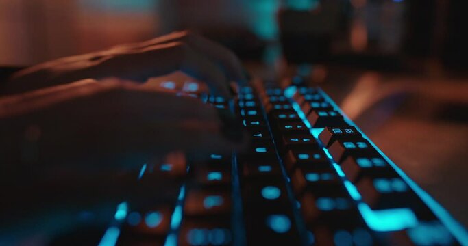 close up hands typing on keyboard programmer coding software gamer using keyboard with blue backlight playing game at night