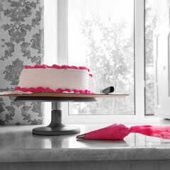 cake making, white cake with pink cream, stands on the table by the window