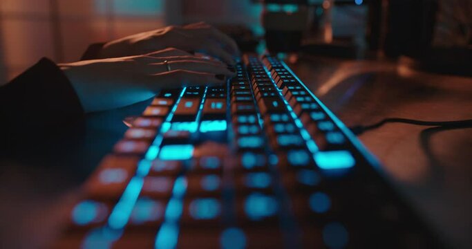 close up hands typing on keyboard programmer coding software gamer using keyboard with blue backlight playing game at night