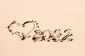The inscription 2022 and the heart are drawn on the light sand. New Year symbol