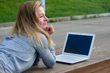 A woman with a laptop lies on a bench and works online