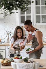 Happy couple making video call with smartphone while preparing dinner in the kitchen at home Cheerful Caucasian people are waving their hands, smiling at the camera, greeting and chatting with friends