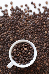 Cup with roasted coffee beans on the background of scattered coffee beans. Top view, copy space. Concept