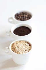 Assorted coffee in white cups, coffee beans, ground and black brewed. White background, copy space.