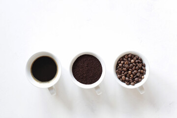 Assorted coffee in white cups, coffee beans, ground and black brewed. White background, copy space. Top view, Concept