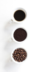 Top view, light background with white cups filled with assorted coffee, coffee beans, ground and black brewed.