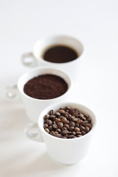 Assorted coffee in white cups, coffee beans, ground and black brewed. White background, copy space.