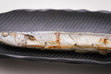 白バックで黒いお皿にのっている焼いた秋刀魚のアップ　fish