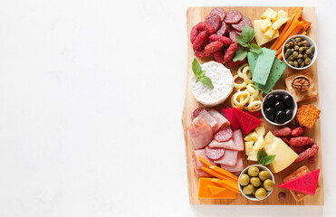 Assorted meat, sausages, cheeses with nuts, olives, croutons on a wooden board. Food on a light background. Top view with copy space. Beautiful serving of snacks. Service delivery, catering.