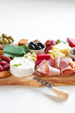 Large wooden board for snacks with different cheeses, meats, sausages, olives, nuts. Nice serving board with meats and cheeses. Vertical on a light background.
Close-up. 