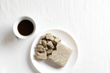 Halva from sunflower seeds in a white plate on a light background. Cup of natural coffee. Copy of space, top view
