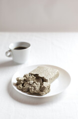 Fototapeta na wymiar Halva from sunflower seeds in a white plate on a light background. Cup of natural coffee.