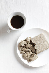 Halva from sunflower seeds in a white plate on a light background. Cup of natural coffee. Copy of space, top view
