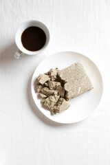 Halva from sunflower seeds in a white plate on a light background. Cup of natural coffee. Copy of space, top view