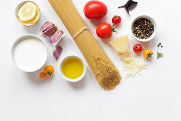 Food ingredients for Italian pasta, spaghetti, fresh farm tomatoes, garlic, peppers, basil, olive oil, Parmesan cheese, lemon, vegetable milk. On white background. Top view with copy space.