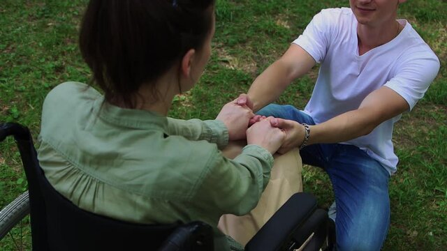 A woman in a wheelchair and her boyfriend on his knees holding hands and talking