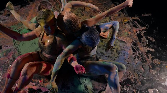 A group of creative elegant female dancers in sportswear improvises in the performance of modern dance, gymnastics and modern dance movements in a black studio paint on their skin