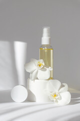 Obraz na płótnie Canvas Vertical image of mock up of glass bottle with essential oil, white jar with cream, orchid flowers. White background with morning rays of sun. Concept of skin care, spa treatments, natural cosmetics