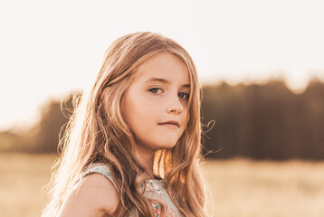 Beautiful little girl blonde with long hair walking through a wheat field