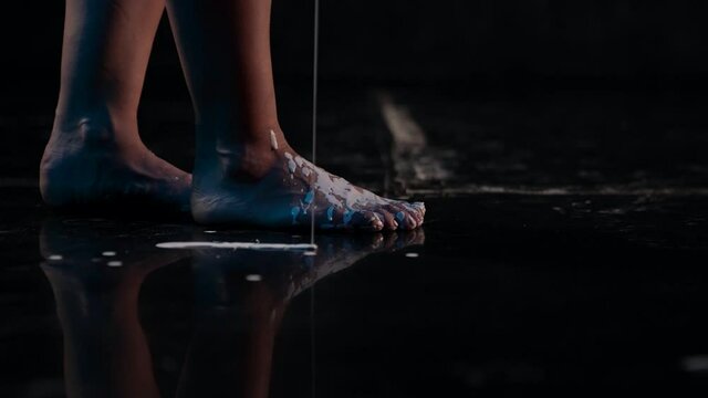 Close-up in the dark of a woman foot walking on a black floor and spilling paint art artist improvisation