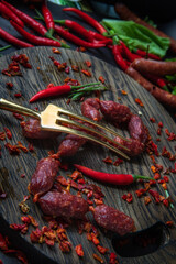 pork fat sausages - salami lying on the wooden cutting board, red hot chili peppers around and paprika, vintage fork on the sausages
