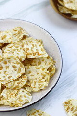 Keripik Tempe or Tempeh Crackers or tempeh chips on ceramic bowl with cup of tea. Tea and snack time. Selective focus, copy space. Indonesian snack.