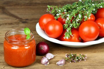 Homemade preserved  ketchup. Jar of fresh ketchup  in front, fresh tomatoes and herbs of basil, thyme and savory at the back.
