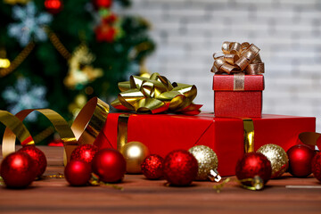 Studio shot of small and big red paper wrapped present gift boxes with gold and silver ribbon bow tie placed on wood table with decorative hanging sphere ball in front full decor Christmas pine tree