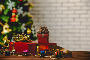Studio shot of small and big red paper wrapped present gift boxes with gold and silver ribbon bow tie placed on wood table with decorative hanging sphere ball in front full decor Christmas pine tree